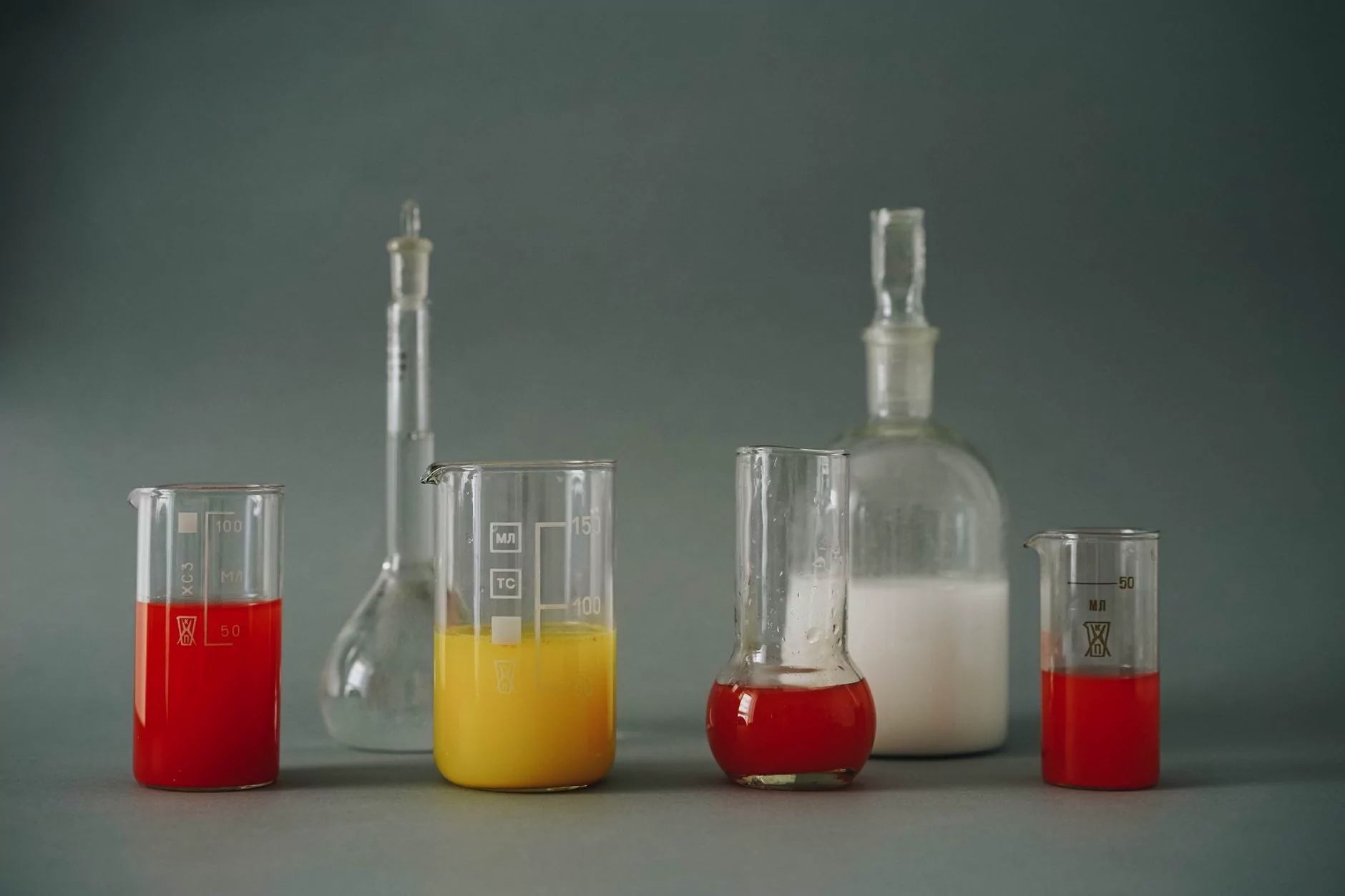Studio shot of colorful laboratory beakers and glassware on gray backdrop.
