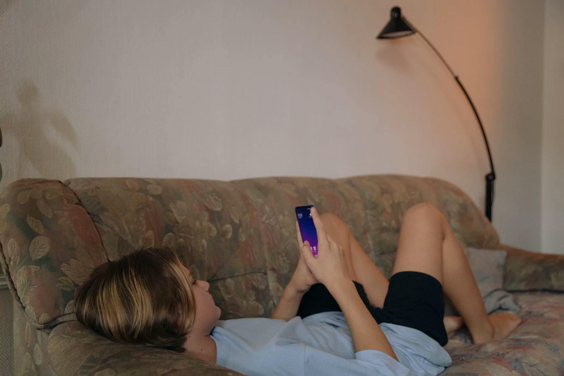 A young woman relaxing on a sofa, using her smartphone. The cozy indoor setting conveys comfort and leisure.